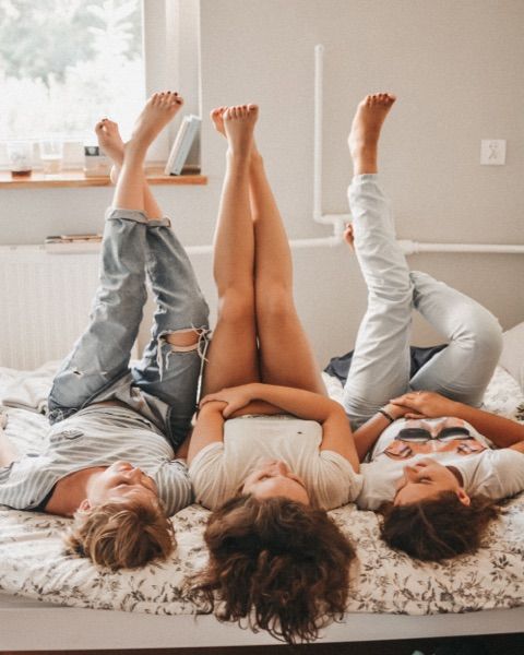 Photo og three woman lying on a bed with their feet in the air