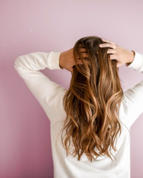 Photo of the back of a woman against a pink background with long brown hair